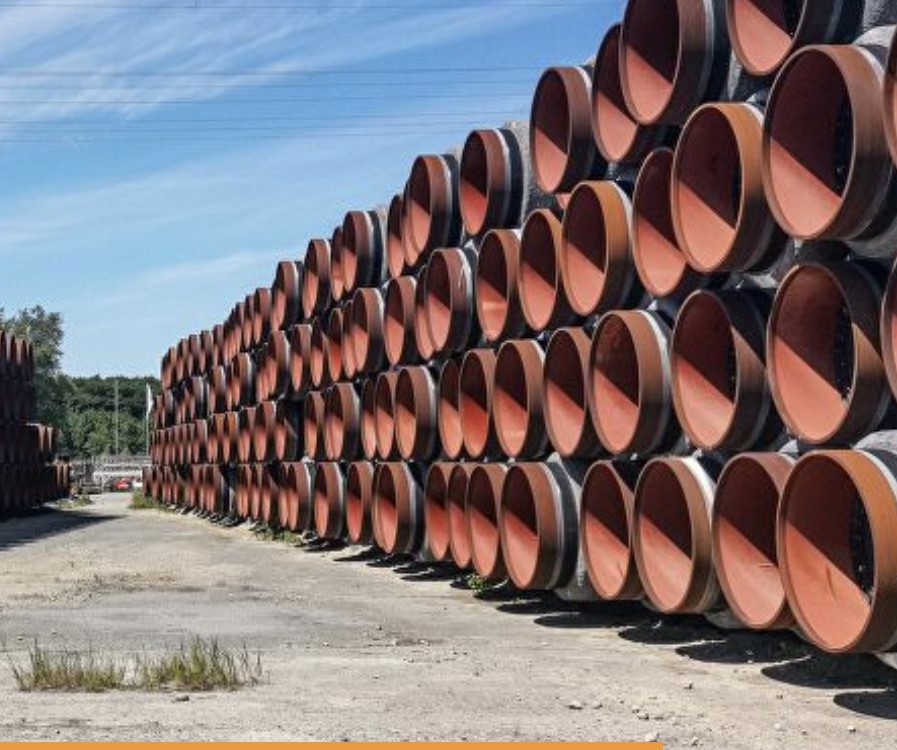 Kusy potrubí naskádaných v řadě na asfaltu