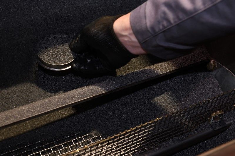 technik sbírá vzorek abraziva železnou miskou ze stroje